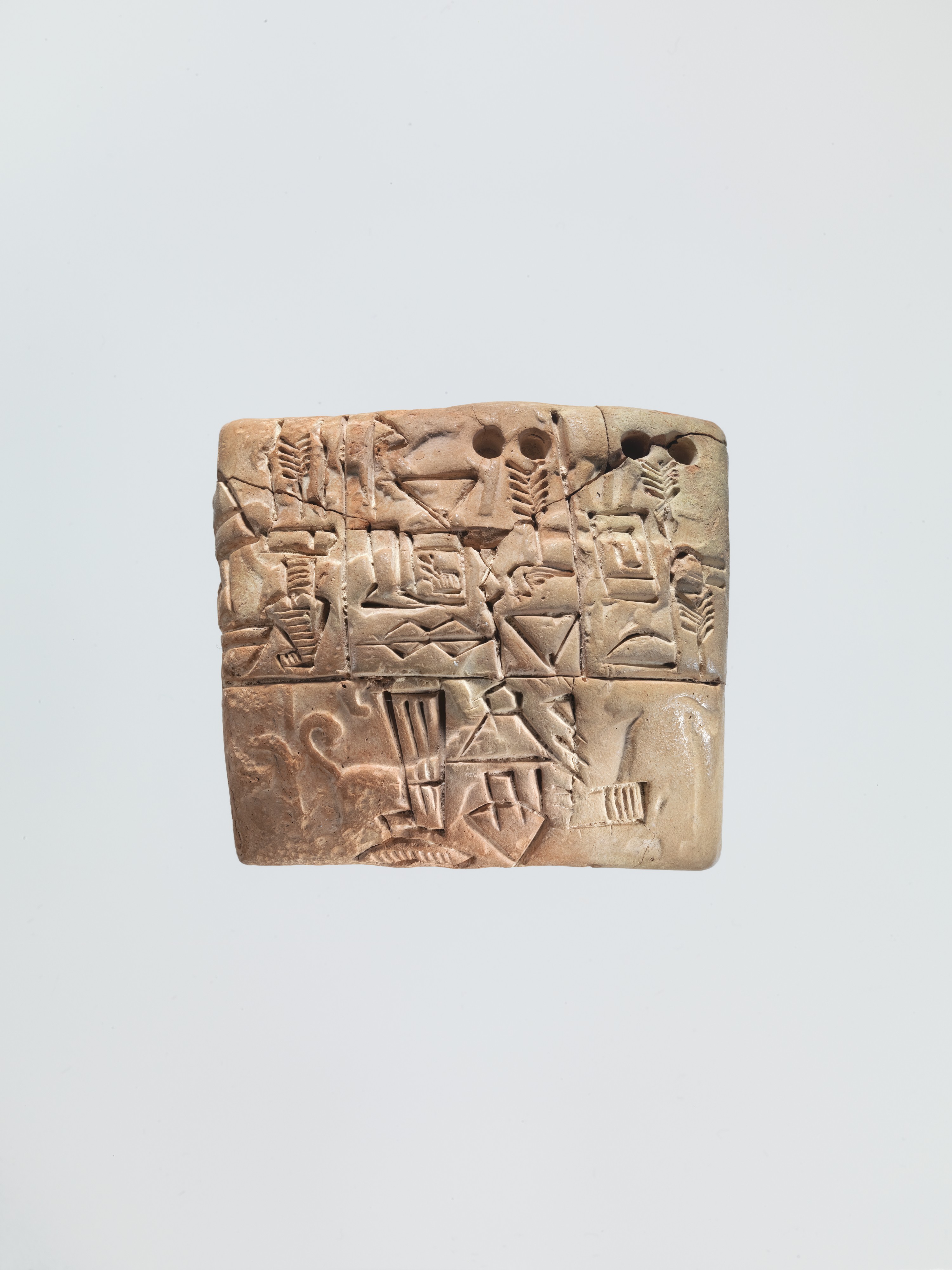 Proto-cuneiform clay tablet with circular impressions, drawn signs, dividing lines and faint seal imagery.