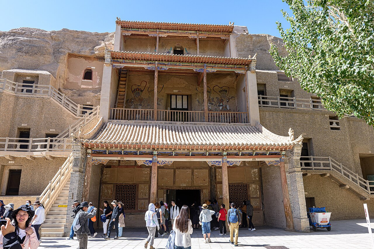 The modern exterior of Caves 16 and 17 at Mogao has doors, numbered signs and a fenced walkway.
