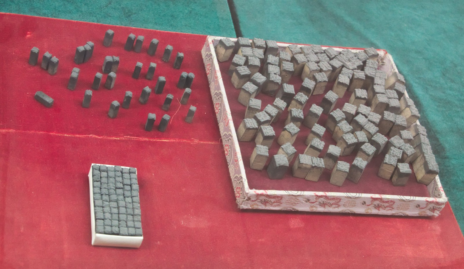 Chinese characters appear on individual wooden blocks in a museum display, some gathered in a tray and others standing separately.