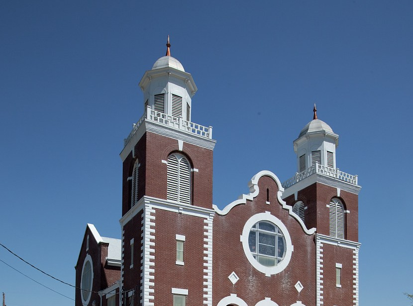 The upper brick facade of Brown Chapel shows two towers, white trim and a circular window against blue sky.