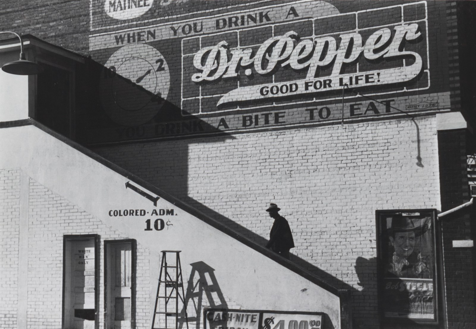 A man climbs cinema steps beside a Colored Admission sign in Belzoni, Mississippi.