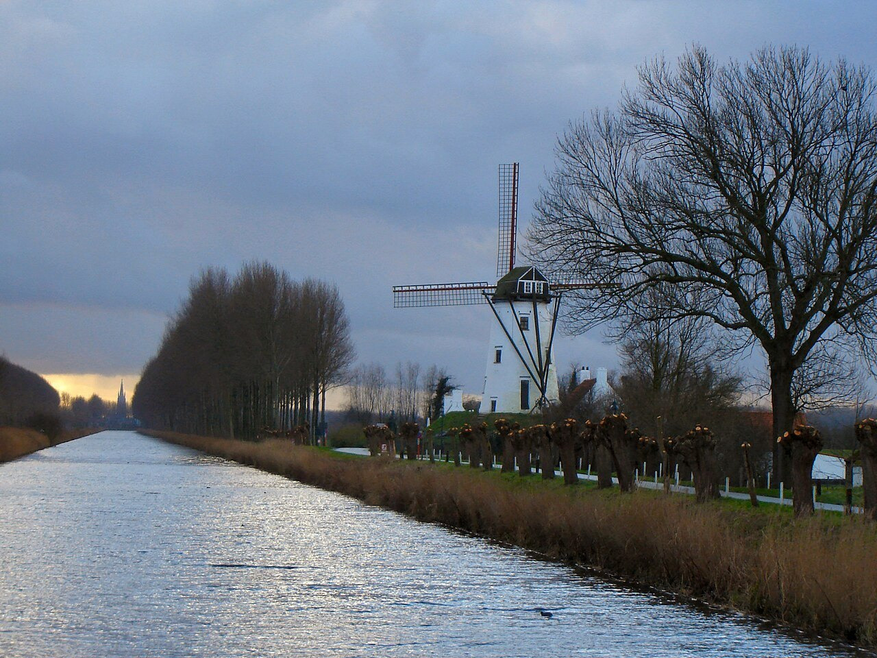 A straight canal at Damme runs beside rows of trees and a white windmill.