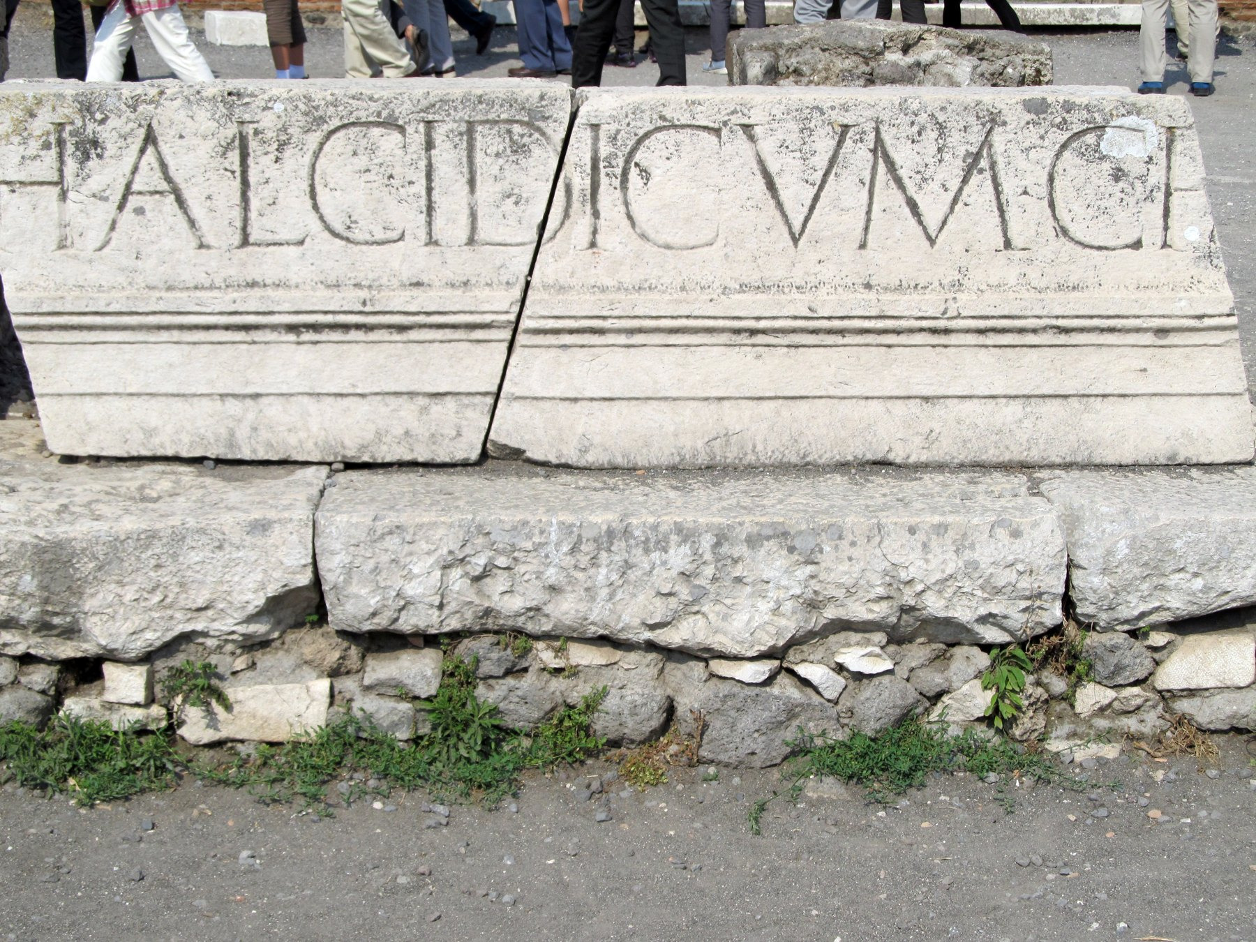 A broken stone entablature carries large Latin letters, including part of the word chalcidicum.