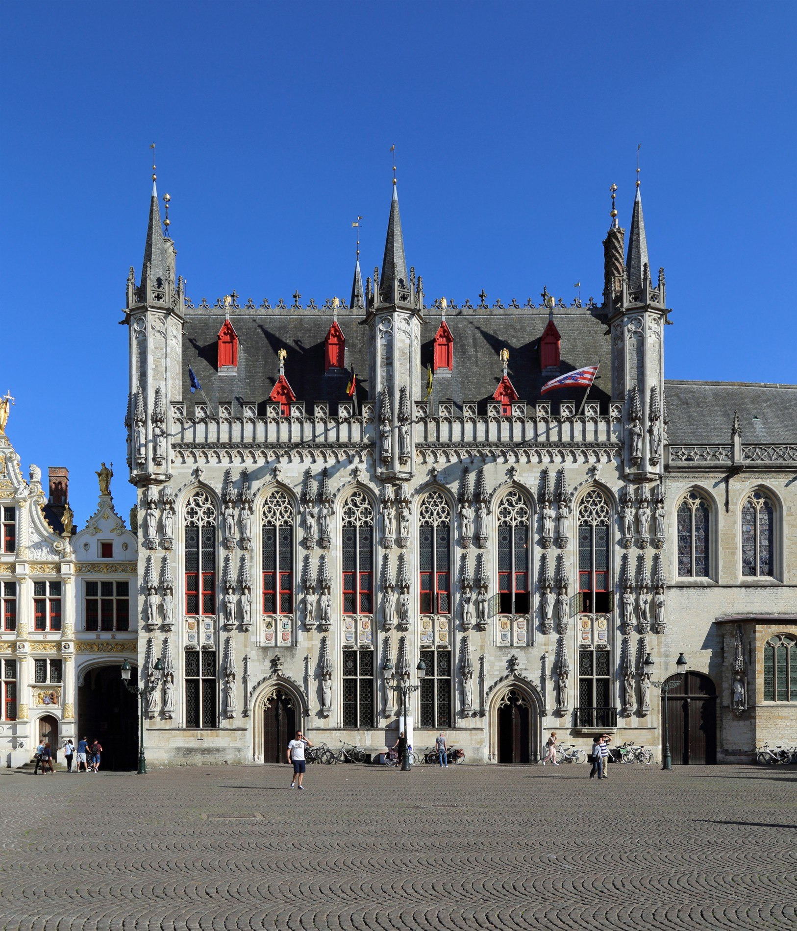 The decorated stone facade of Bruges town hall, with windows, statues and slender towers.