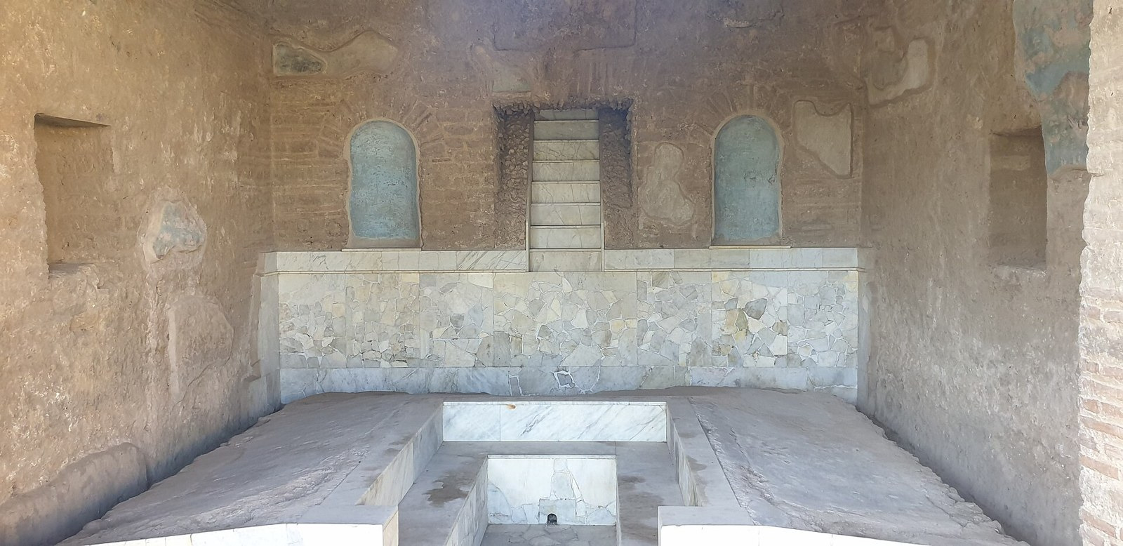 Stone dining couches surround a table beneath a decorated garden-facing recess.