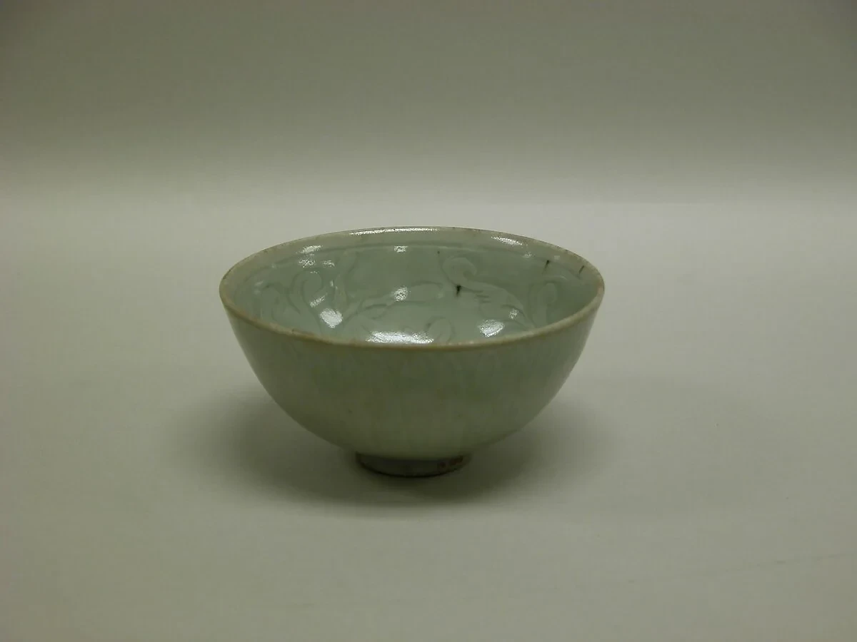 A pale green glazed bowl with floral decoration is photographed against a dark background.