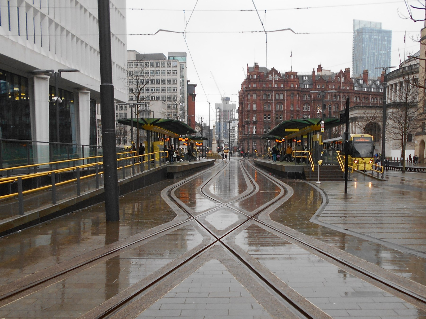 A modern photograph shows wet tram tracks and buildings around Manchester’s St Peter’s Square.