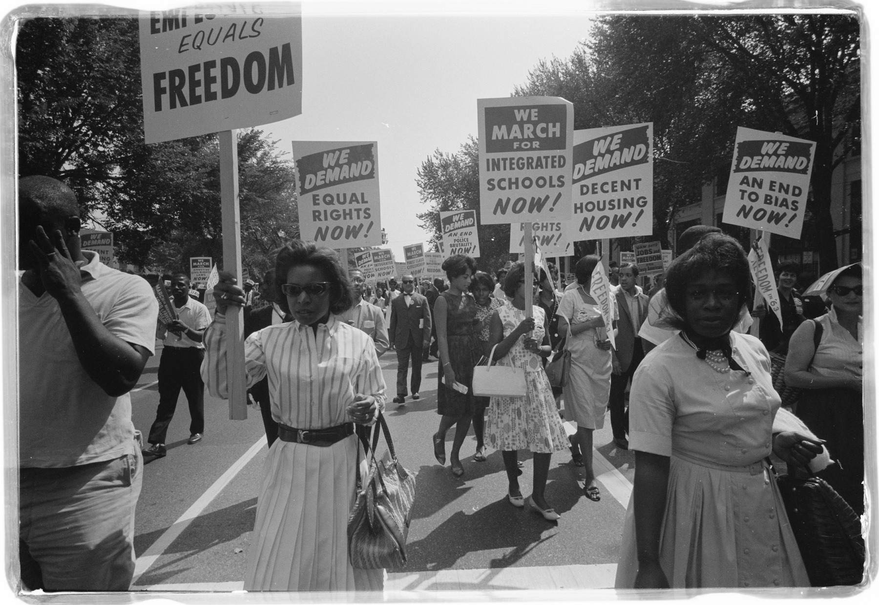 Marchers walk together carrying placards for integrated schools, an end to bias and decent housing.