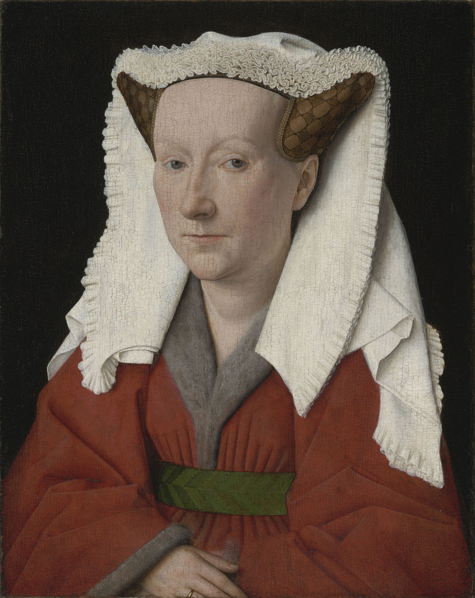 Margaret van Eyck faces the viewer, wearing a white head covering, red clothing and a fur collar against a dark background.