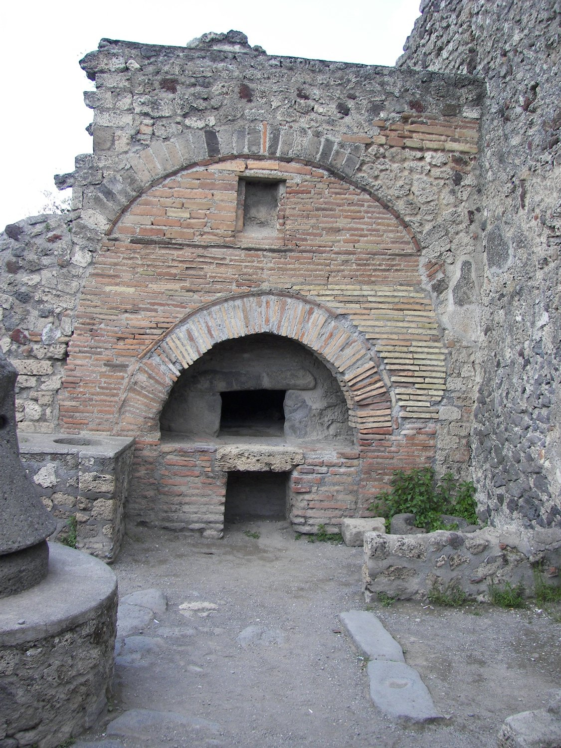 A masonry oven has an arched brick front and a dark rectangular opening in its cooking chamber.