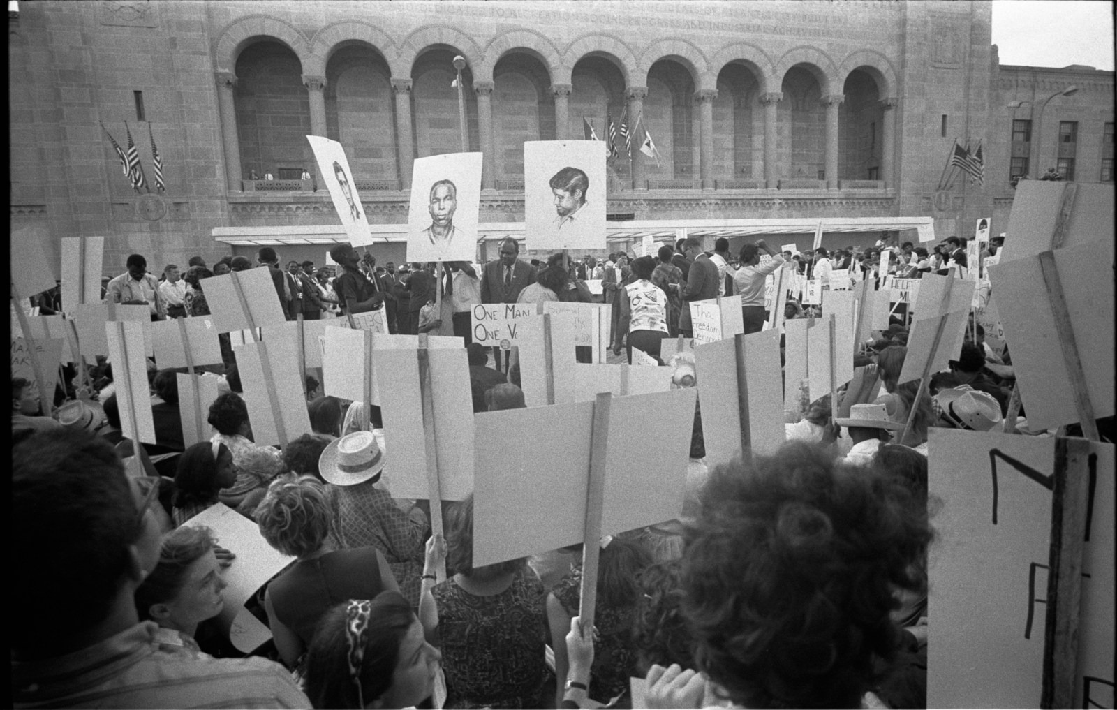 A crowd outside the convention holds placards, including portraits of murdered civil rights workers.