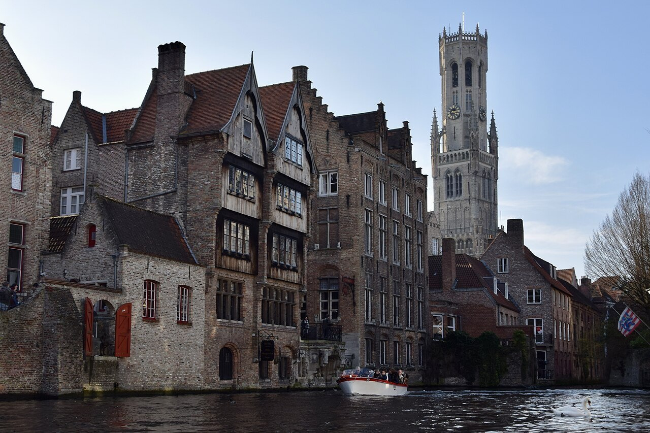 Water in front of brick buildings at the Rozenhoedkaai, with the Bruges belfry beyond.